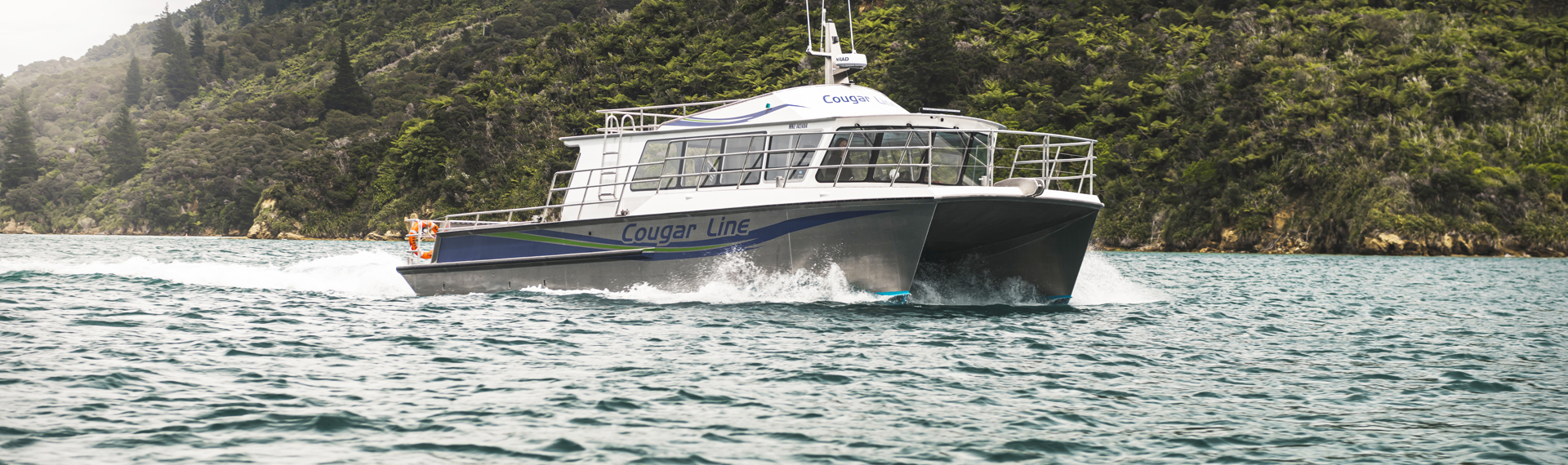 The name on the side of Cougar Line's Sounds Exciting boat sits above the boat's wake, while cruising the Marlborough Sounds, New Zealand