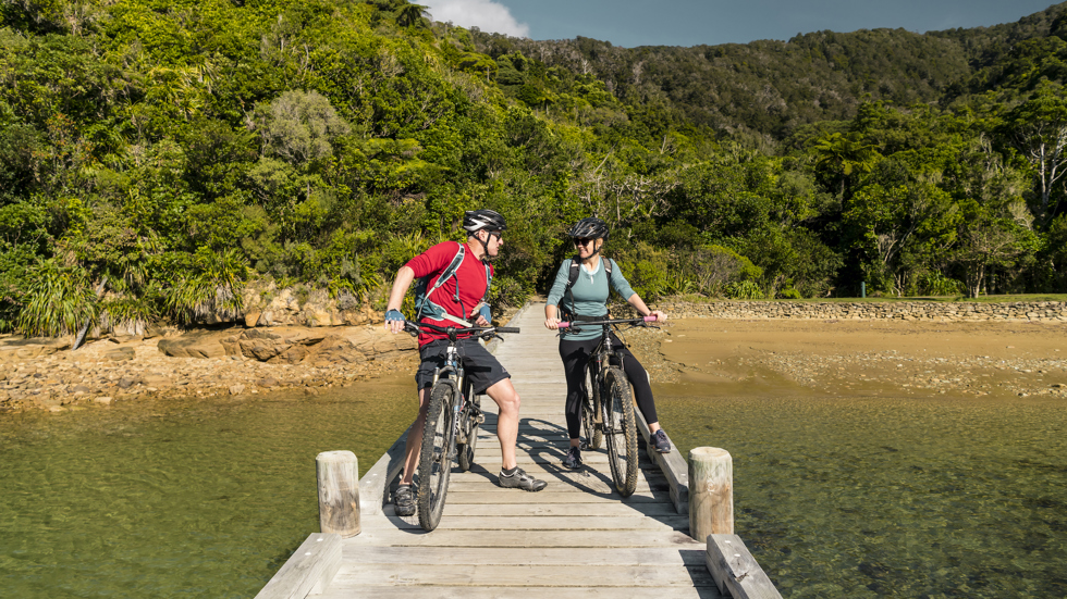 A couple on mountain bikes on the jetty at Ship Cove/Meretoto, Marlborough Sounds, New Zealand.