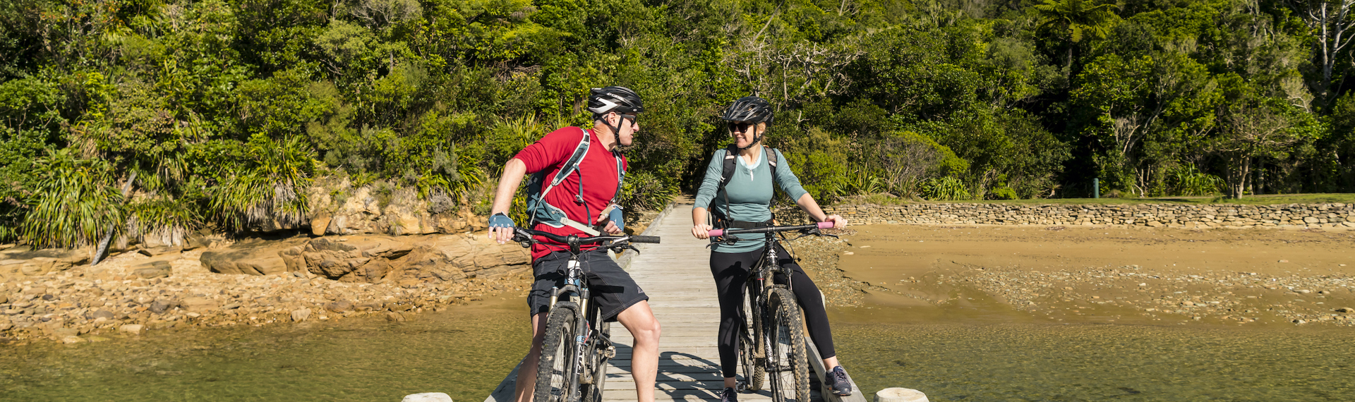 A couple on mountain bikes on the jetty at Ship Cove/Meretoto, Marlborough Sounds, New Zealand.