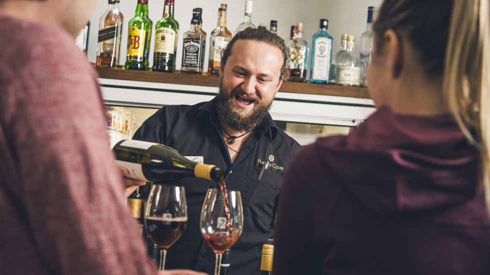 A Punga Cove staff member pours red wine for two people at the Boatshed Café & Bar in the Marlborough Sounds, New Zealand.