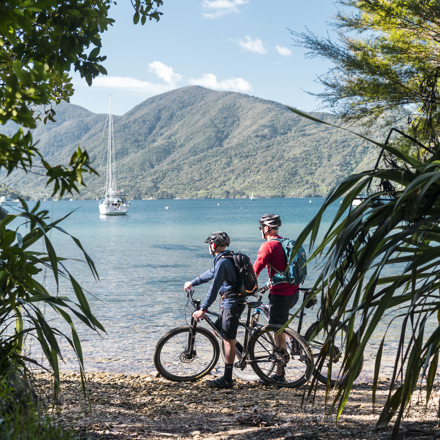 Mountain bikers stop on a beach on the northern Queen Charlotte Track in the Marlborough Sounds, New Zealand.