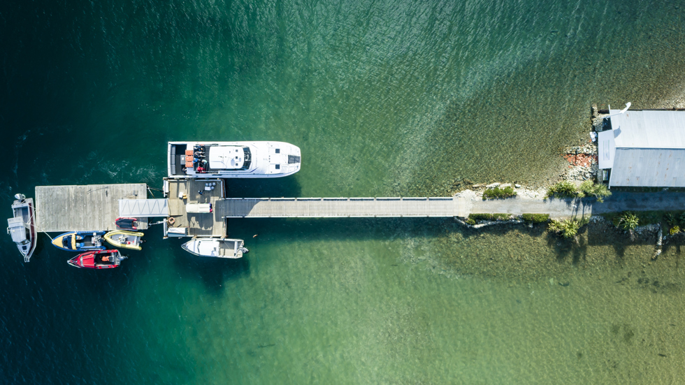 An aerial view of the Furneaux Lodge jetty, boat shed, Cougar Line boat and smaller boats in the Marlborough Sounds, New Zealand.